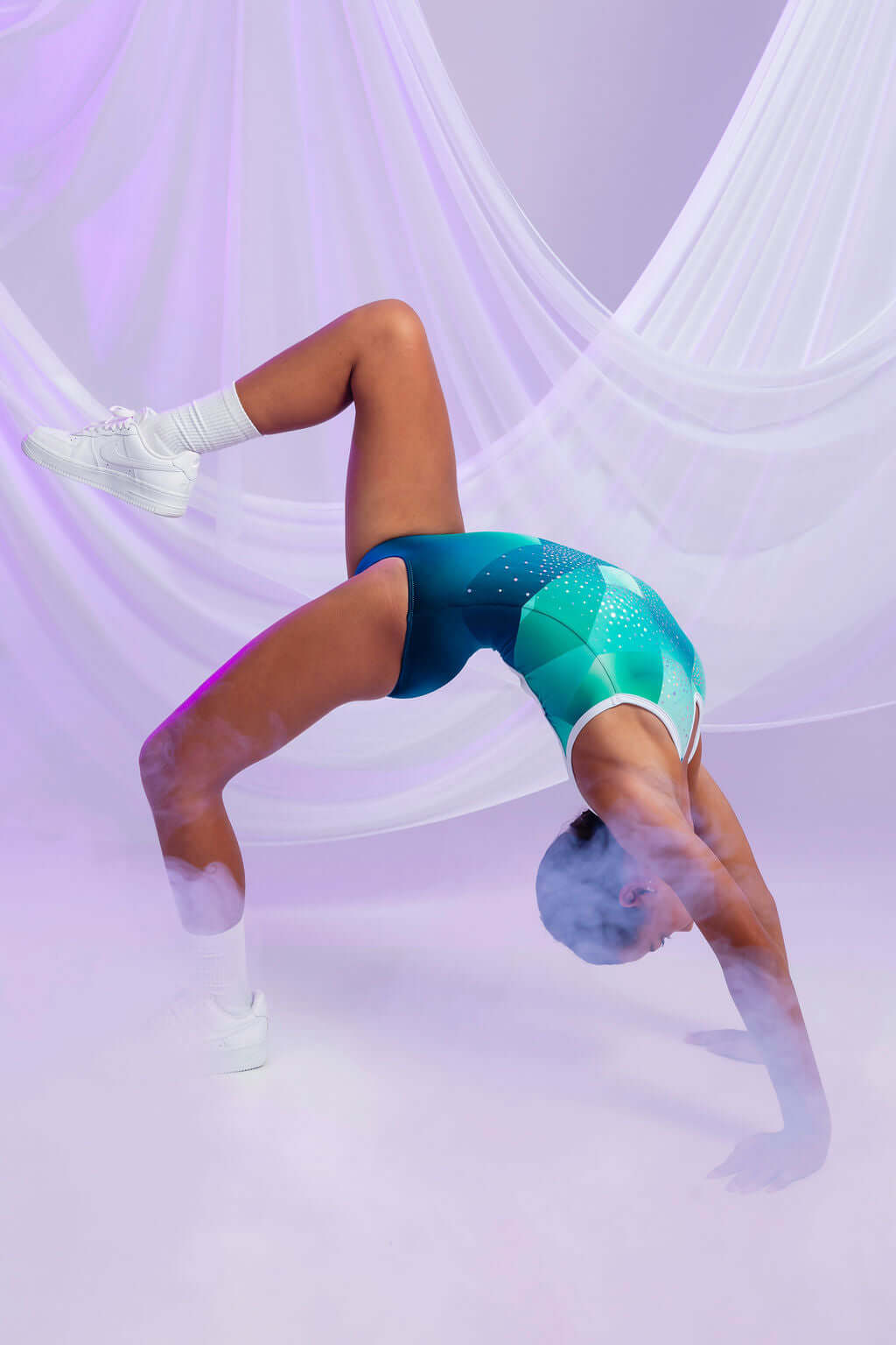 Athlete performing a breathtaking backbend in a vibrant green Marina Del Rey leotard against a misty background.