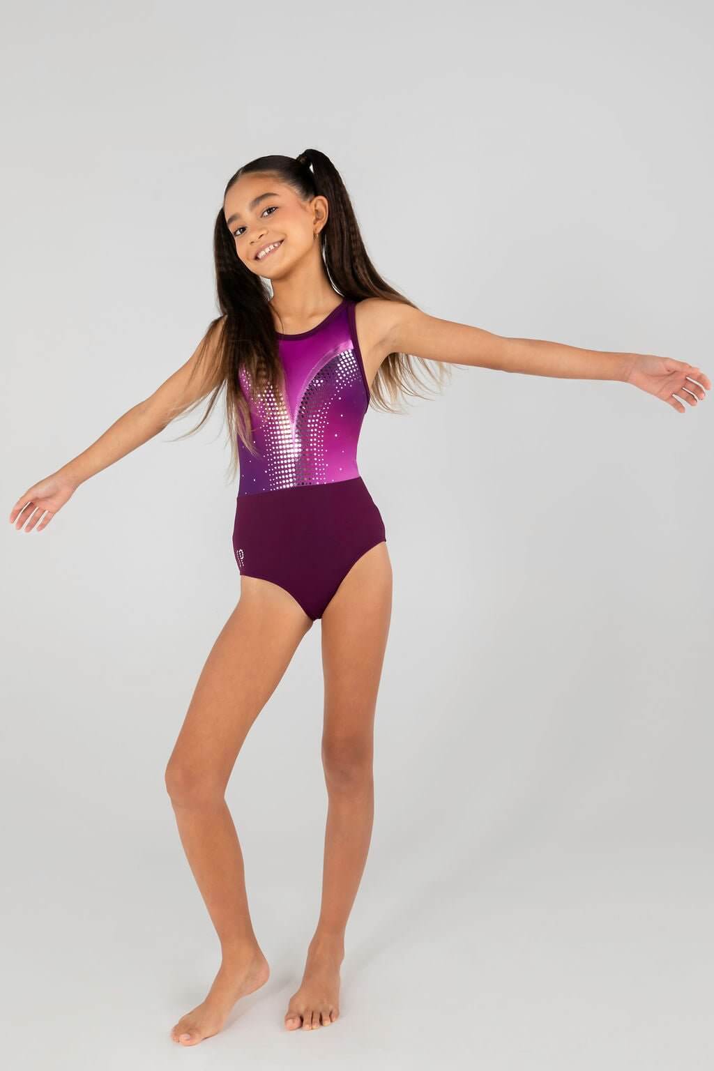 Girl in Glitz N Glam Leotard with dark plum hues and boysenberry shimmer, posing with arms outstretched.