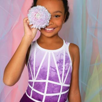 Young girl in the Misha leotard from the From Paris with Love Collection, playfully holding a flower against her face, set against a colorful backdrop.