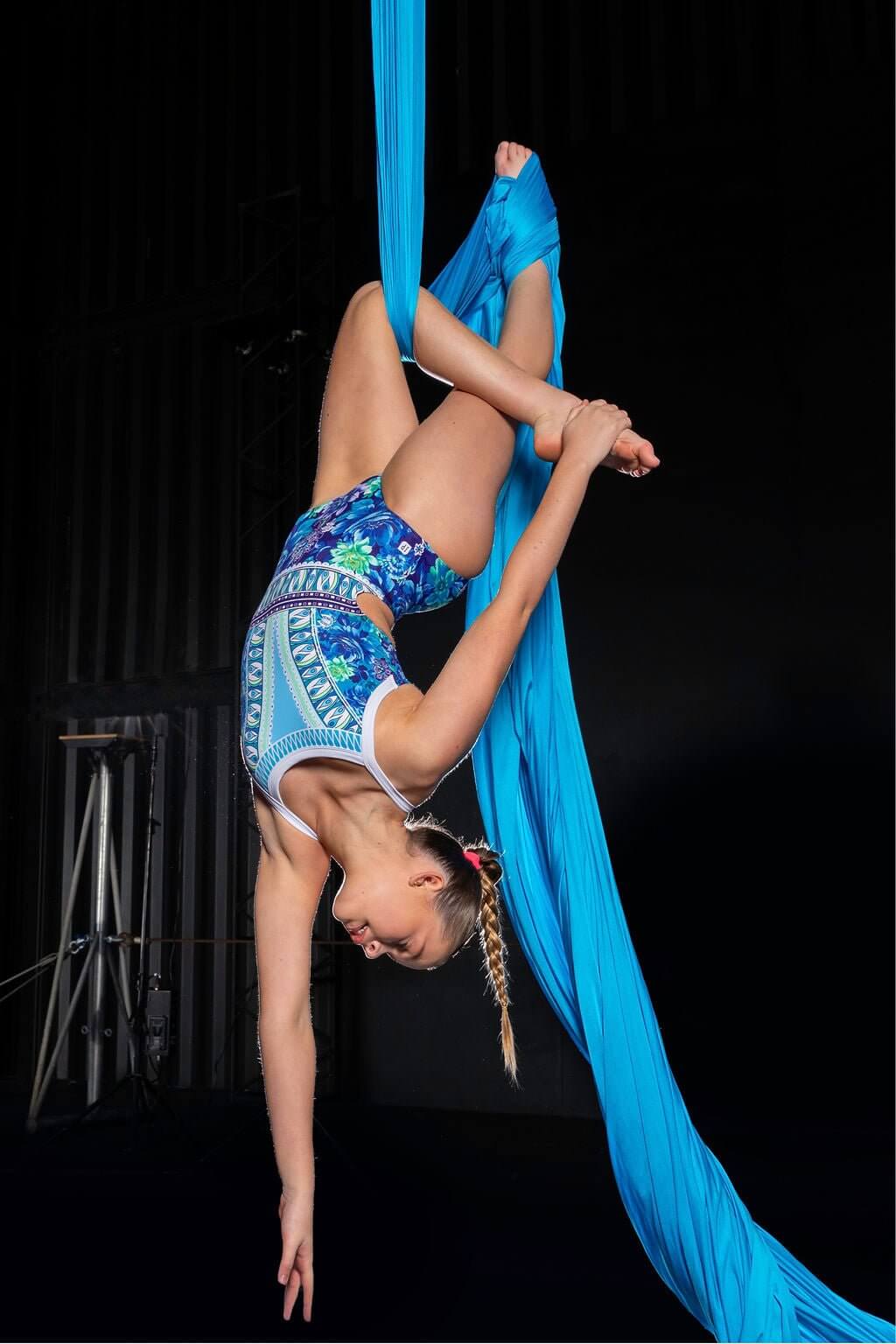 Aerial performer in stylish leotard, showcasing flexibility and grace while suspended in vibrant blue silks.