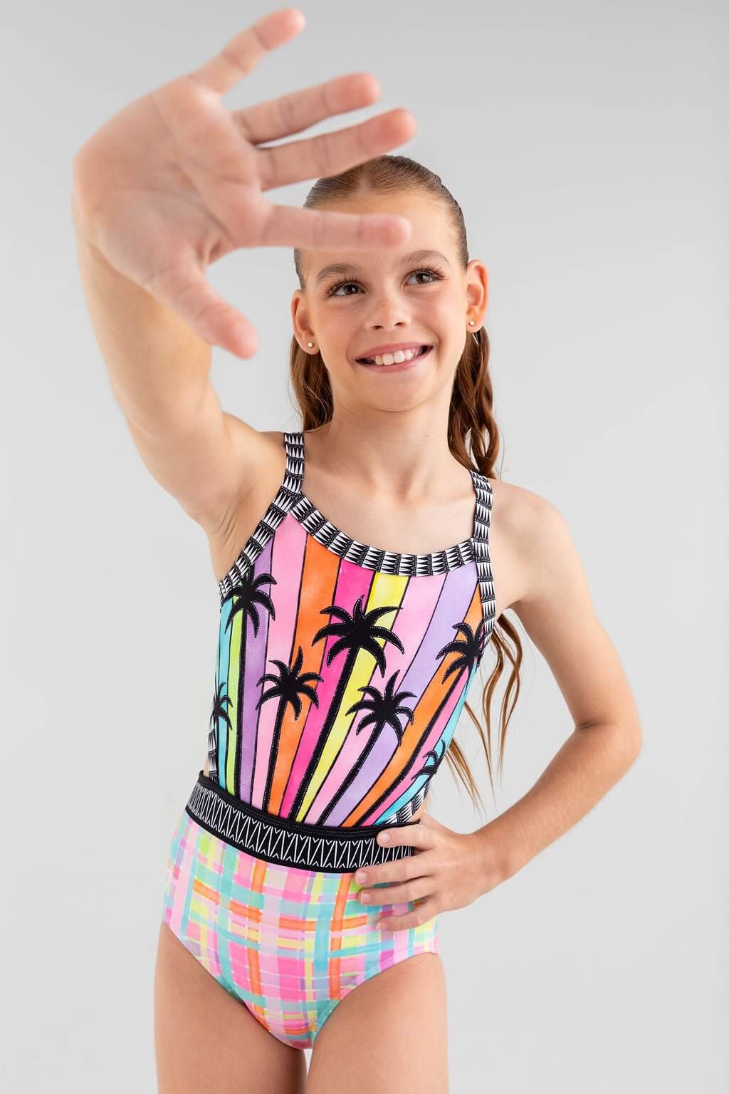 Girl in Mademoiselle Leotard with colorful palm tree print, playful pose, joyfully showcasing vibrant design.